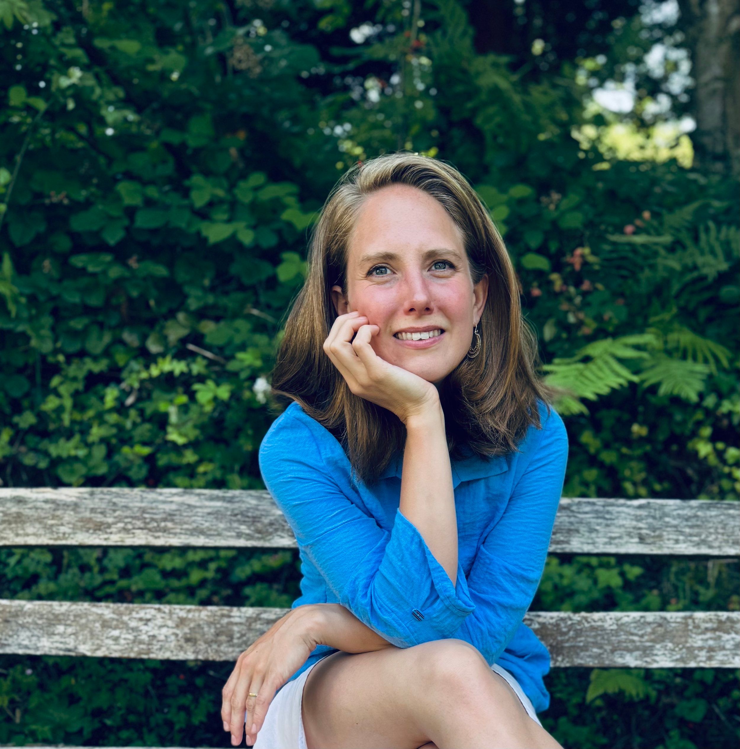 Katherine Kaufmann in a blue shirt on a garden bench in front of green leaves